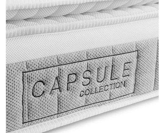 Close-up of a white quilted mattress with a gray woven label on the side that reads 'CAPSULE COLLECTION'.