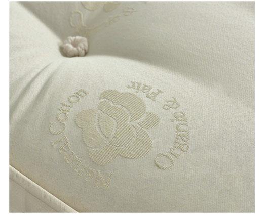 Close-up of a cream-colored tufted mattress or cushion fabric with an embroidered logo featuring a flower and the words 'Cotton Pura' and 'Made in Mexico'.