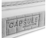 Close-up of a white quilted mattress with a gray woven label on the side that reads 'CAPSULE COLLECTION'.