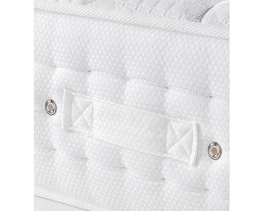 Close-up of a white quilted mattress or cushion with tufted texture, a central fabric strap, and two metal rivets on a white background.