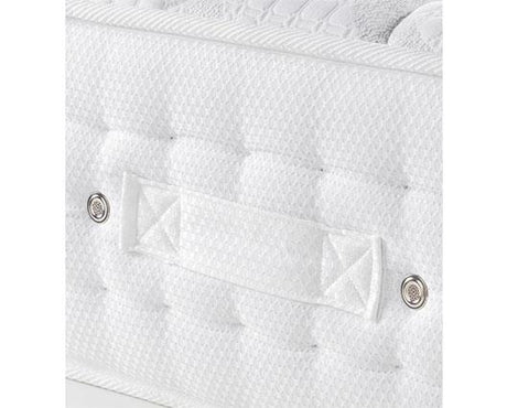 Close-up of a white quilted mattress or cushion with tufted texture, a central fabric strap, and two metal rivets on a white background.
