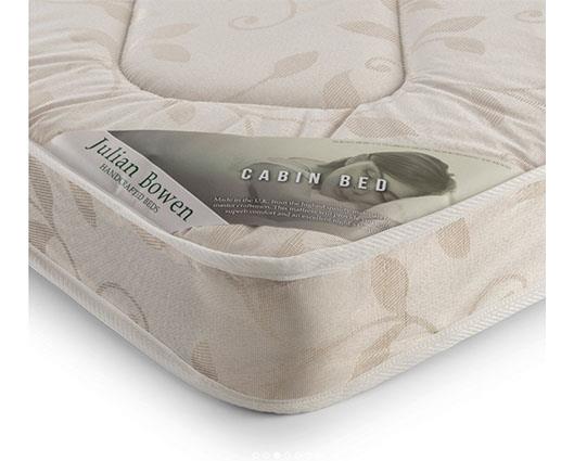 A close-up of a mattress corner showing a beige fabric cover with a subtle leaf pattern and a paper label that reads 'Julian Bowen' and 'CABIN BED'.
