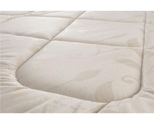 Close-up of a quilted mattress topper or mattress surface in a warm off-white/cream color with a subtle leaf pattern.