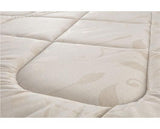 Close-up of a quilted mattress topper or mattress surface in a warm off-white/cream color with a subtle leaf pattern.