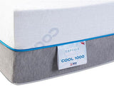 Close-up of a mattress corner showing a white top surface, a gray textured side, a blue seam line, and a white product label reading CAPSULE COOL 1000.