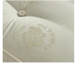 Close-up of a cream-colored tufted mattress or cushion fabric with an embroidered logo featuring a flower and the words 'Cotton Pura' and 'Made in Mexico'.