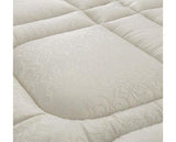 A close-up of a quilted mattress cover in a warm off-white/cream color, showing a subtle woven floral pattern on the central panel.