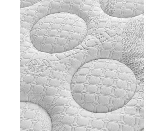 Close-up of a white quilted mattress topper with circular tufted patterns and a subtle leaf motif.