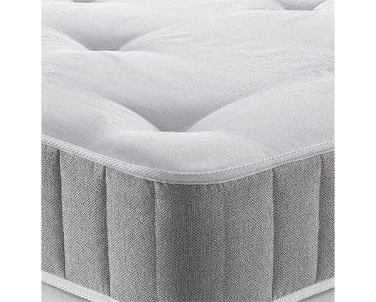 A close-up of a mattress showing its white tufted top surface and light gray textured side skirt.