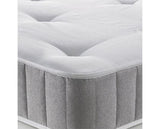 A close-up of a mattress showing its white tufted top surface and light gray textured side skirt.